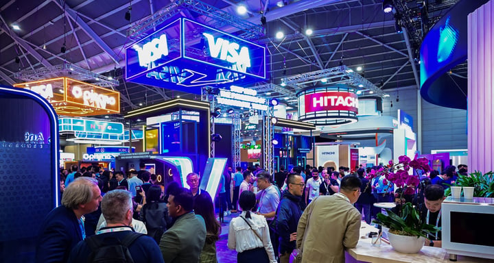 A crowded exhibition aisle at Singapore EXPO under the Visa and Hitachi stands