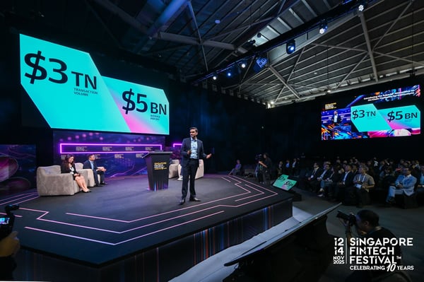 A speaker on stage in front of screens reading $3TN and $5BN