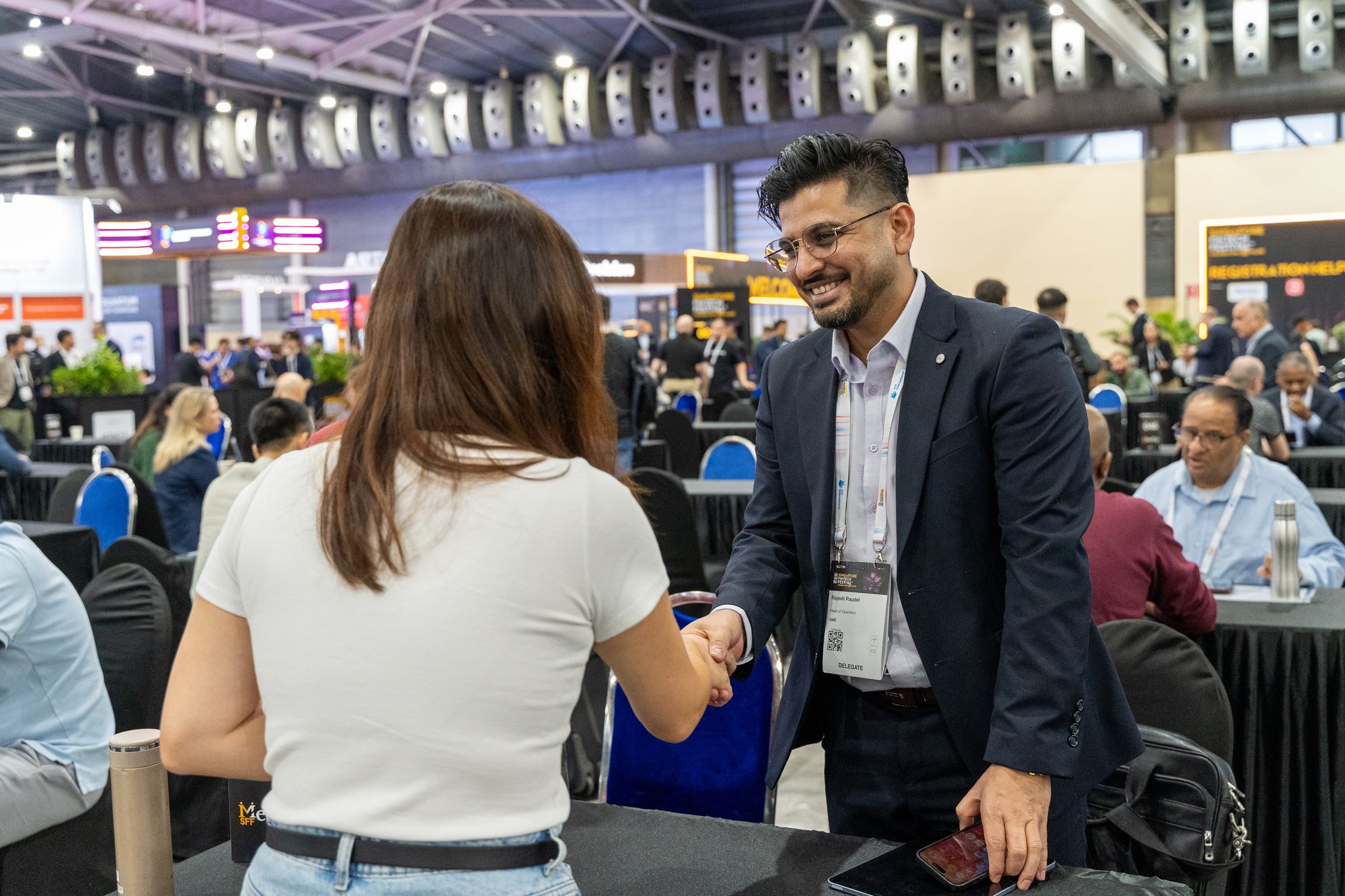 Two attendees shaking hands across a numbered table in the SFF MeetUp area at SFF 2025