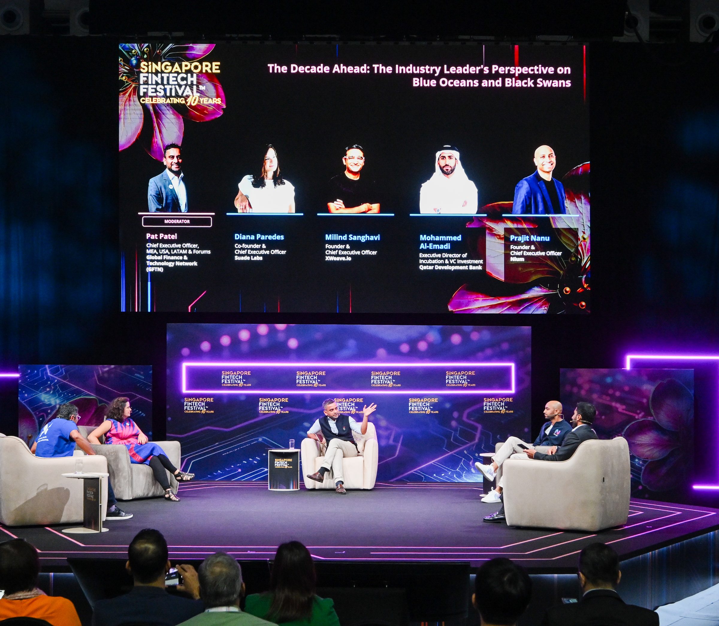 A panel on stage beneath a screen showing the session title and its five speakers